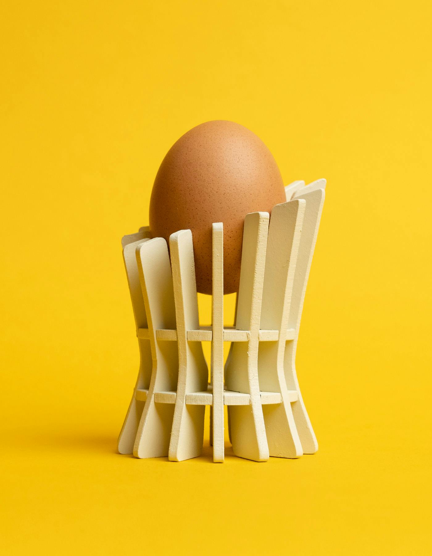 A white cylindrical fin loft model holding up an egg against a bright yellow background.